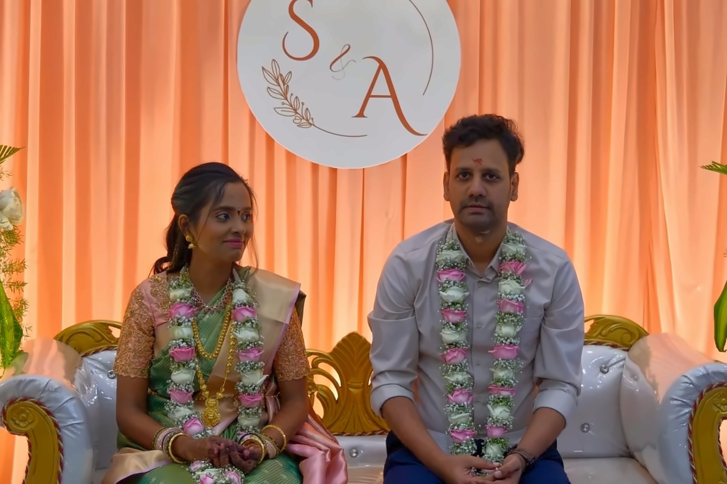 Sindhu and Anand on stage, garlanded, in front of their S & A monogram